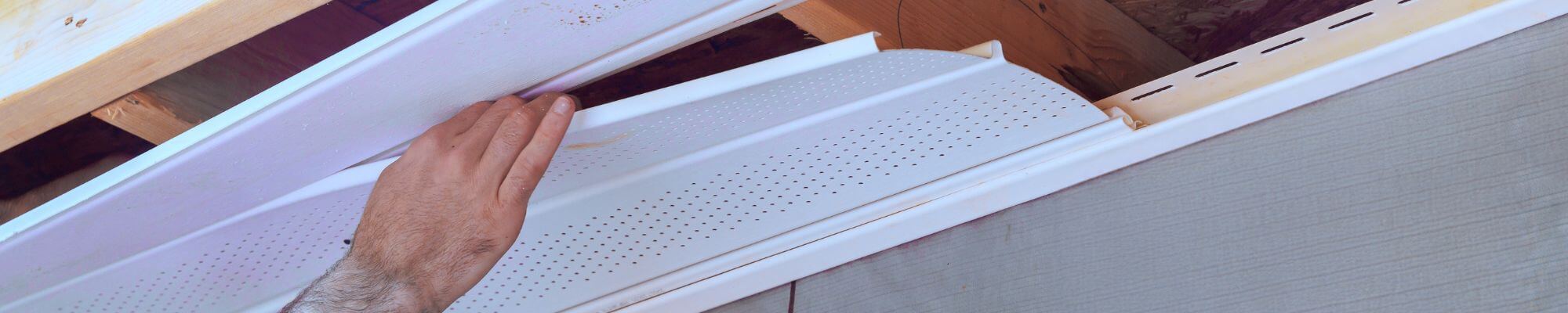 Un professionnel installe un soffite ventilé blanc sous un avant-toit afin d’améliorer l’aération de la toiture.